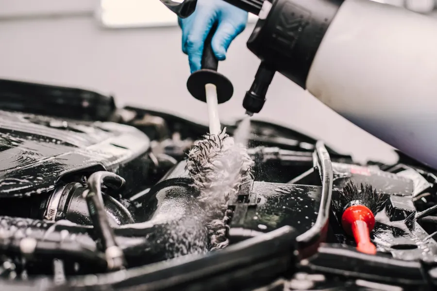 Reiniger wird mit Drucksprüher und Detailbürste auf den eingeschäumten Motorraum aufgebracht