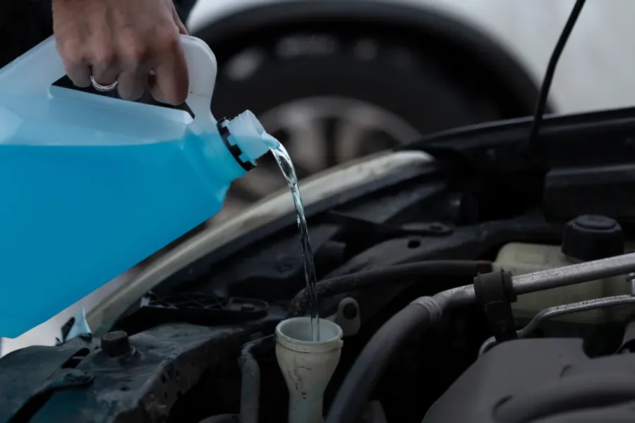 Blaues Scheibenwischwasser wird aus einem Kanister in den Einfüllstutzen im Motorraum gegossen