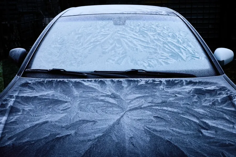 Mit Eisblumen überzogene Frontscheibe und Motorhaube eines Autos an einem Wintermorgen