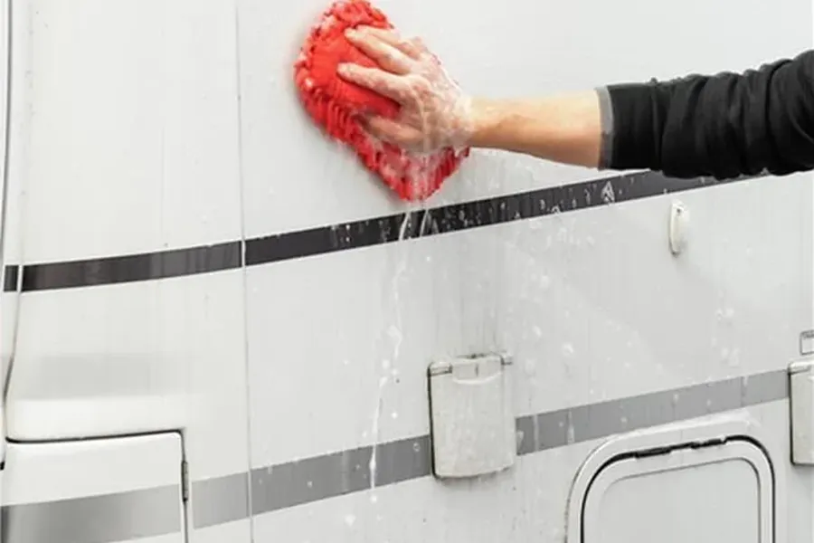 Seitenwand eines Wohnwagens wird mit Waschhandschuh und Schaum gereinigt