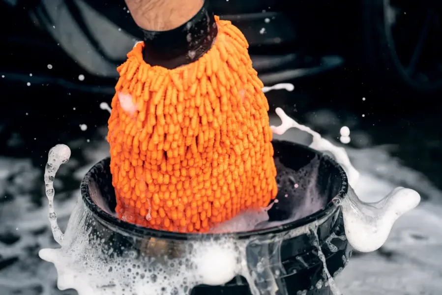 Waschhandschuh wird in einen Eimer mit Shampooschaum getaucht