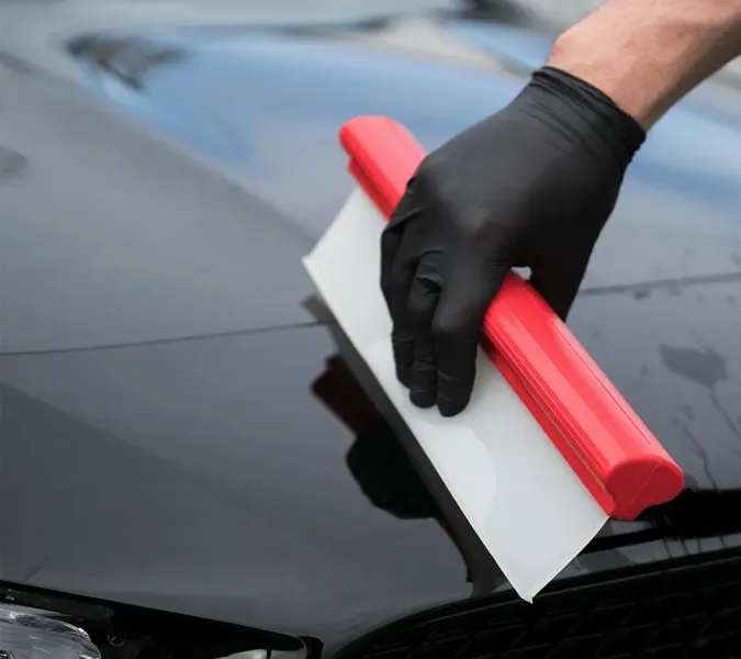 Roter Wasserabzieher wird über eine nasse schwarze Motorhaube gezogen