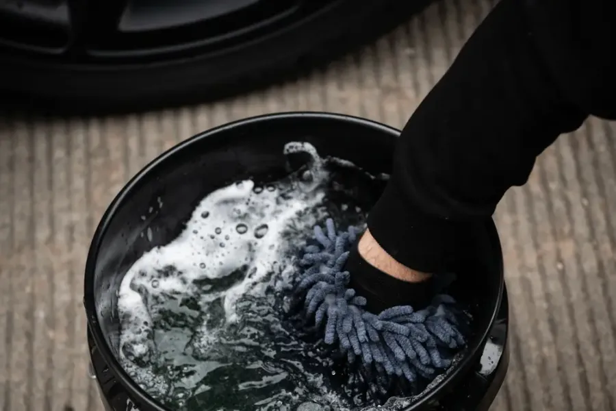 Waschhandschuh wird im Eimer mit Shampooschaum ausgewaschen