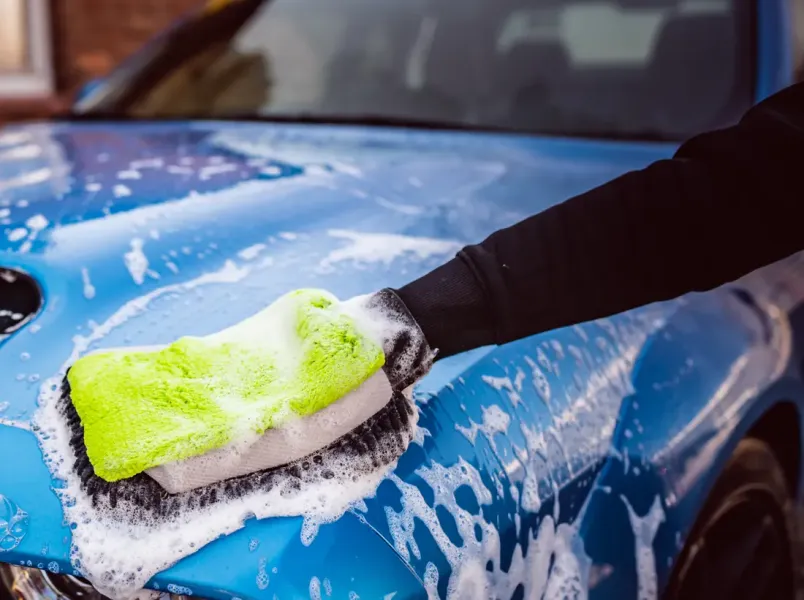Waschhandschuh mit Schaum auf einer blauen Motorhaube