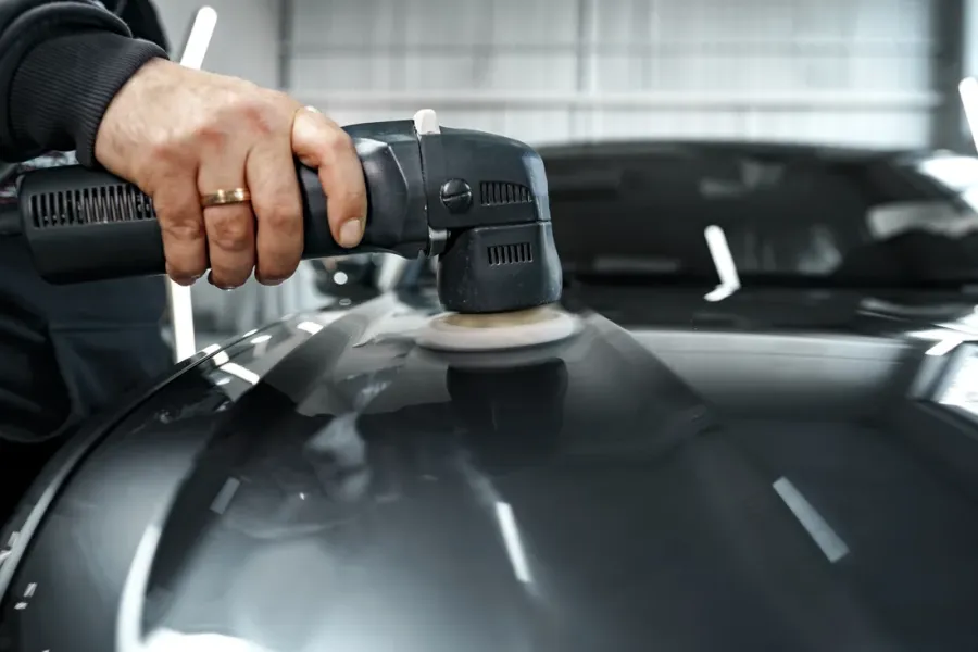 Behandschuhte Hand führt eine Poliermaschine über die schwarze Motorhaube eines Autos