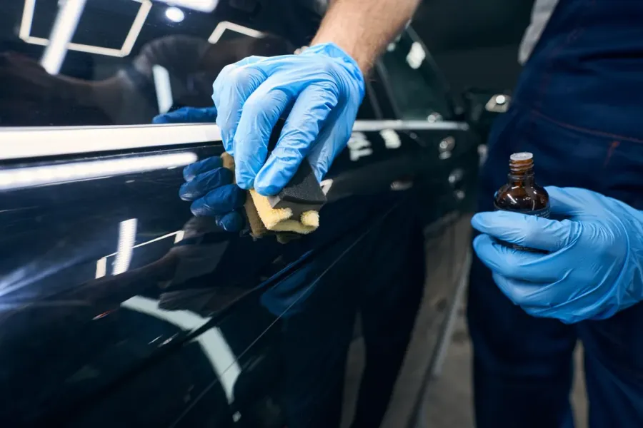 Hand mit Applikator verteilt eine Versiegelung auf schwarzem Autolack